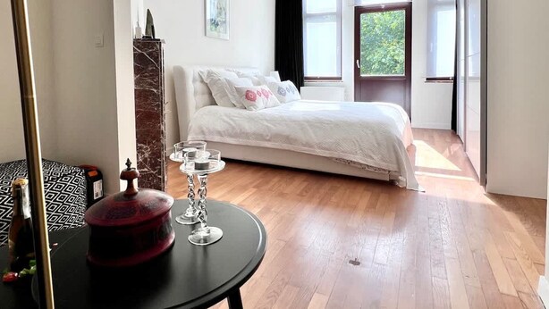 Une chambre à coucher moderne avec un lit, une table avec des verres, une lampe et une vue sur l’extérieur.