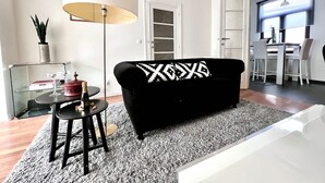 Un salon moderne avec un canapé noir, une table ronde surmontée d’une lampe et un meuble vitré.