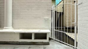 Une cour avec un banc blanc, une porte en métal et un mur en briques.
