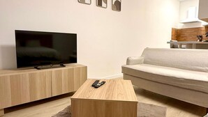 Un salon moderne avec un téléviseur à écran plat, un canapé, une table basse et un coin cuisine à l’arrière-plan.