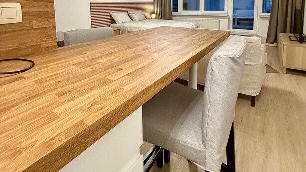 Une chambre d’hôtel moderne avec une table à manger en bois, un lit avec une tête de lit, une fenêtre avec des rideaux et un téléviseur posé sur une table d’appoint.