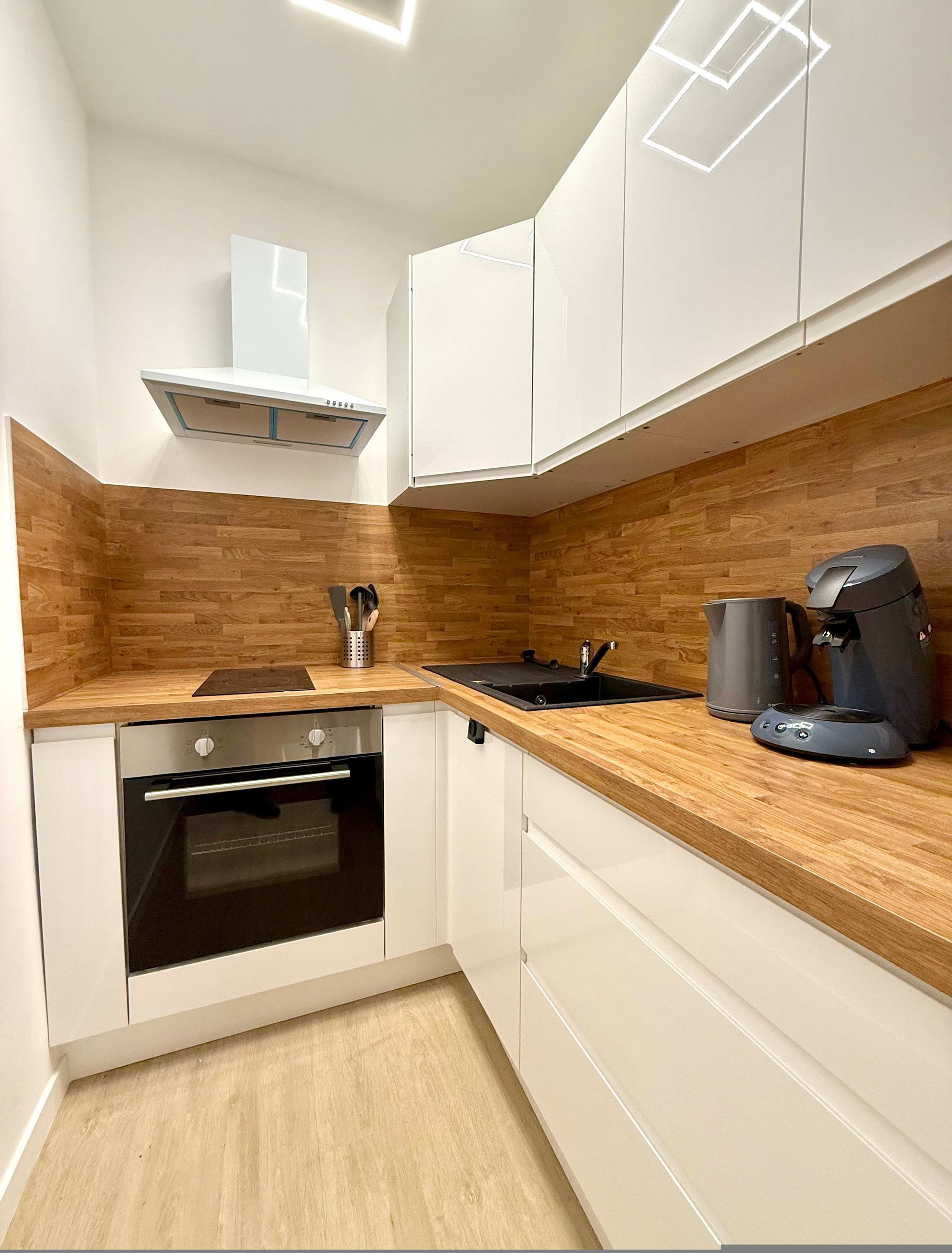Een moderne keuken met witte kasten, een houten aanrecht, een inbouwoven en een koffieapparaat.
