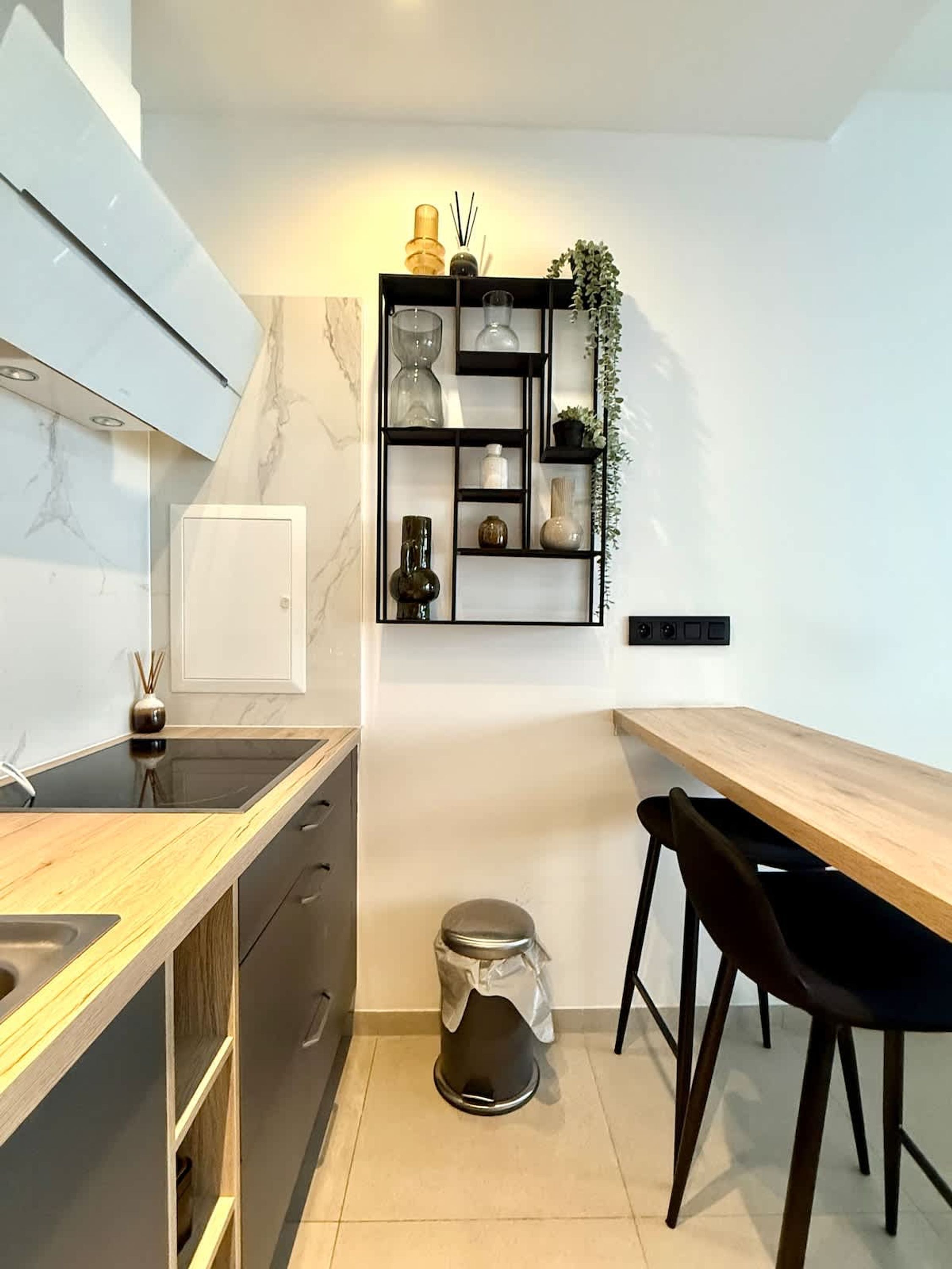 Cozinha moderna com revestimento de mármore, bancada de madeira, uma cadeira preta e prateleira na parede com objetos decorativos.