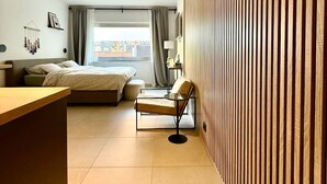 Ett modernt hotellrum med en säng, en stol, ett skrivbord och utsikt över staden.