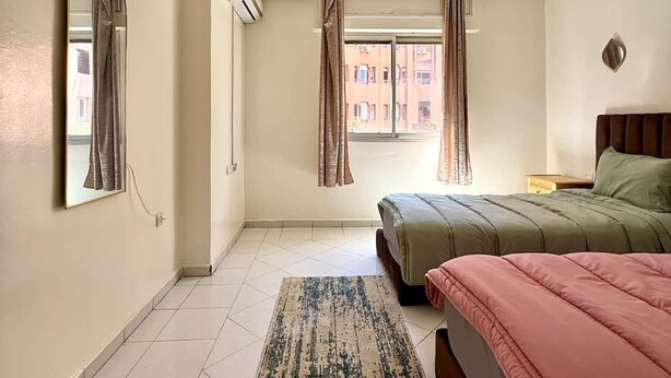 Ein Schlafzimmer mit Bett, Spiegel, einem fenster mit Vorhängen, Teppich und Klimaanlage.