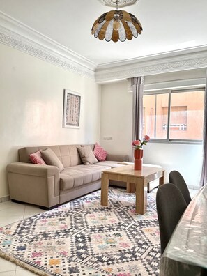 Ein Wohnzimmer mit einem beigen Sofa, einem gemusterten Teppich, einem Holztisch und einer dekorativen Deckenleuchte.