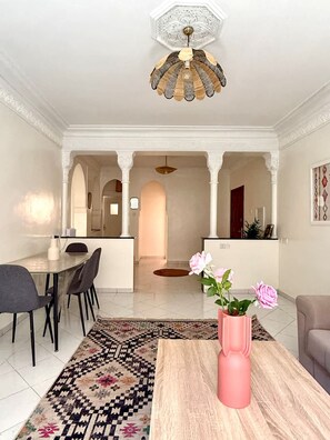 Ein großzügiger Wohnbereich mit Esstisch, Stühlen, einem Couchtisch mit Blumenvase und einem gemusterten Teppich.