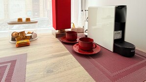 Una habitación con una mesa de madera, un objeto rojo, una cafetera y vistas a edificios a través de una ventana.