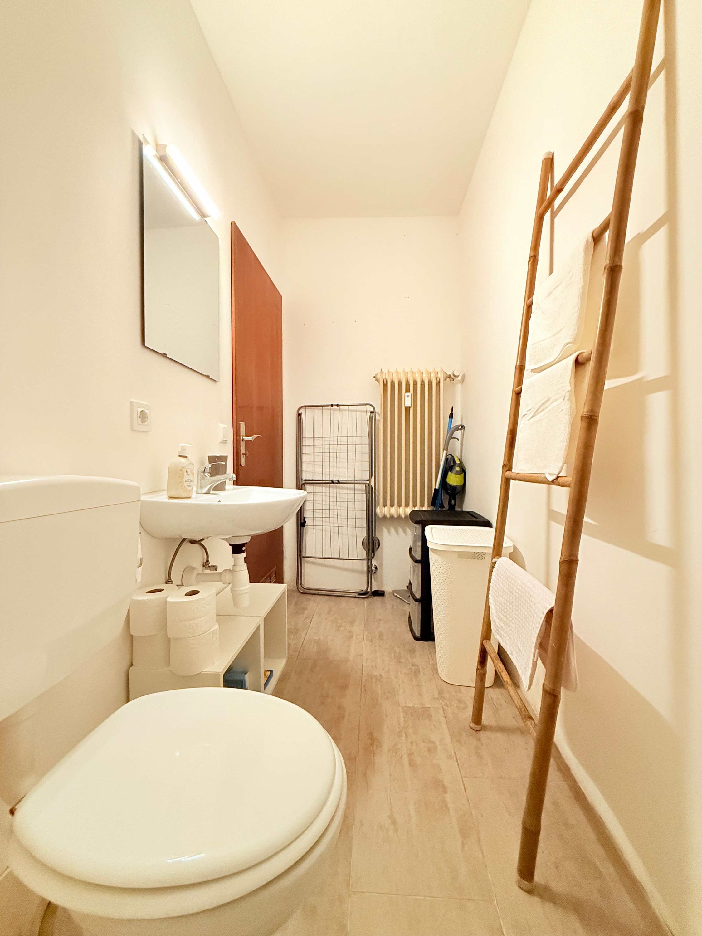 A bathroom with a toilet, sink, mirror, and a wooden ladder.