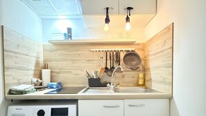 Cocina compacta con lavadora, pileta y utensilios colgantes.
