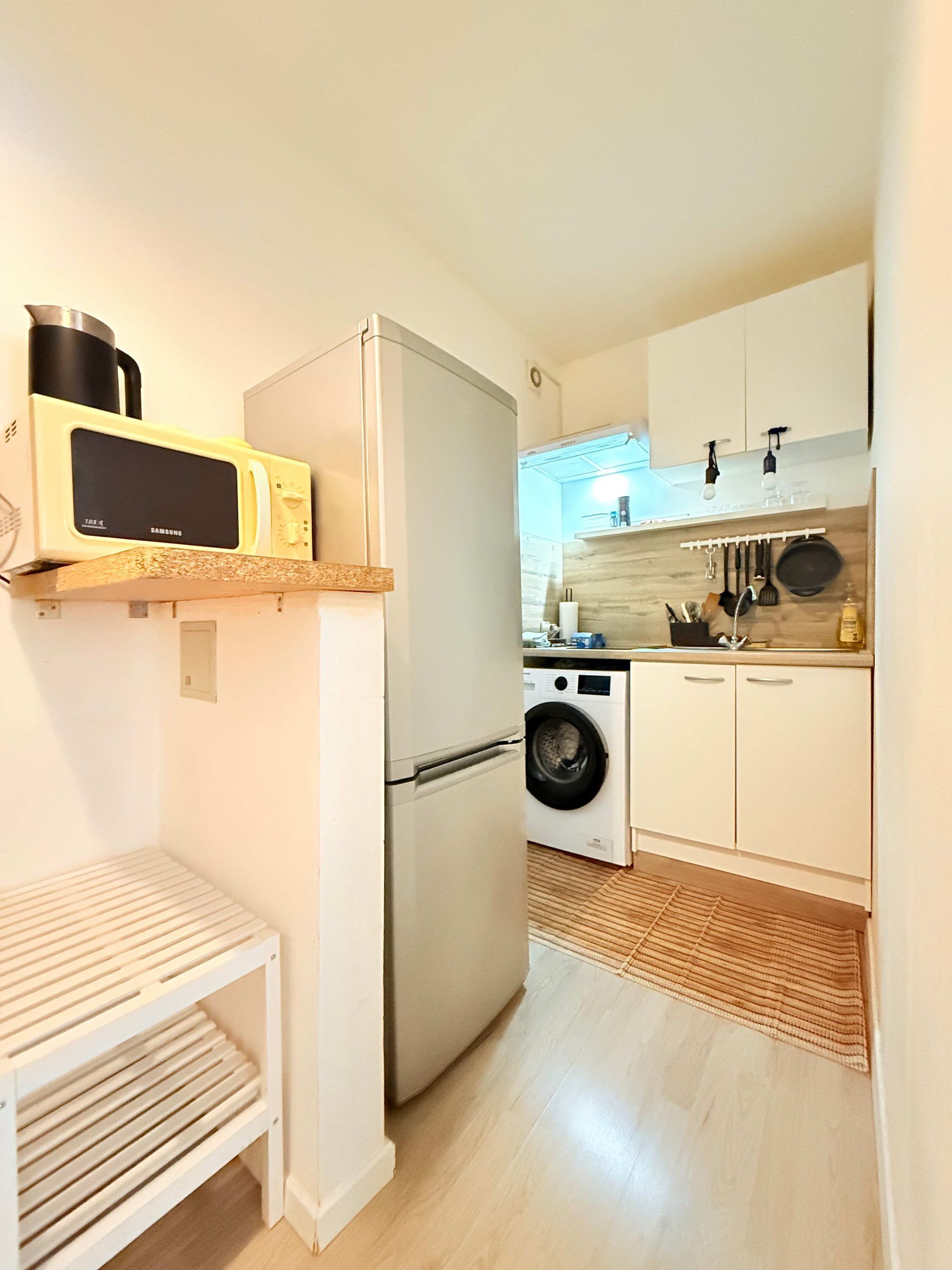 Une cuisine compacte équipée d’un four à micro-ondes, d’un réfrigérateur, d’un lave-linge et d’une petite table.