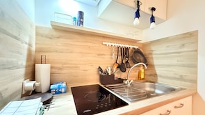 Una cocina con tope de inducción negro, un lavabo, utensilios colgantes y un salpicadero de madera.