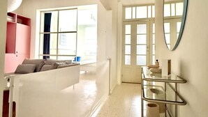 Une pièce spacieuse avec un canapé blanc, une étagère en verre et un grand miroir au mur.