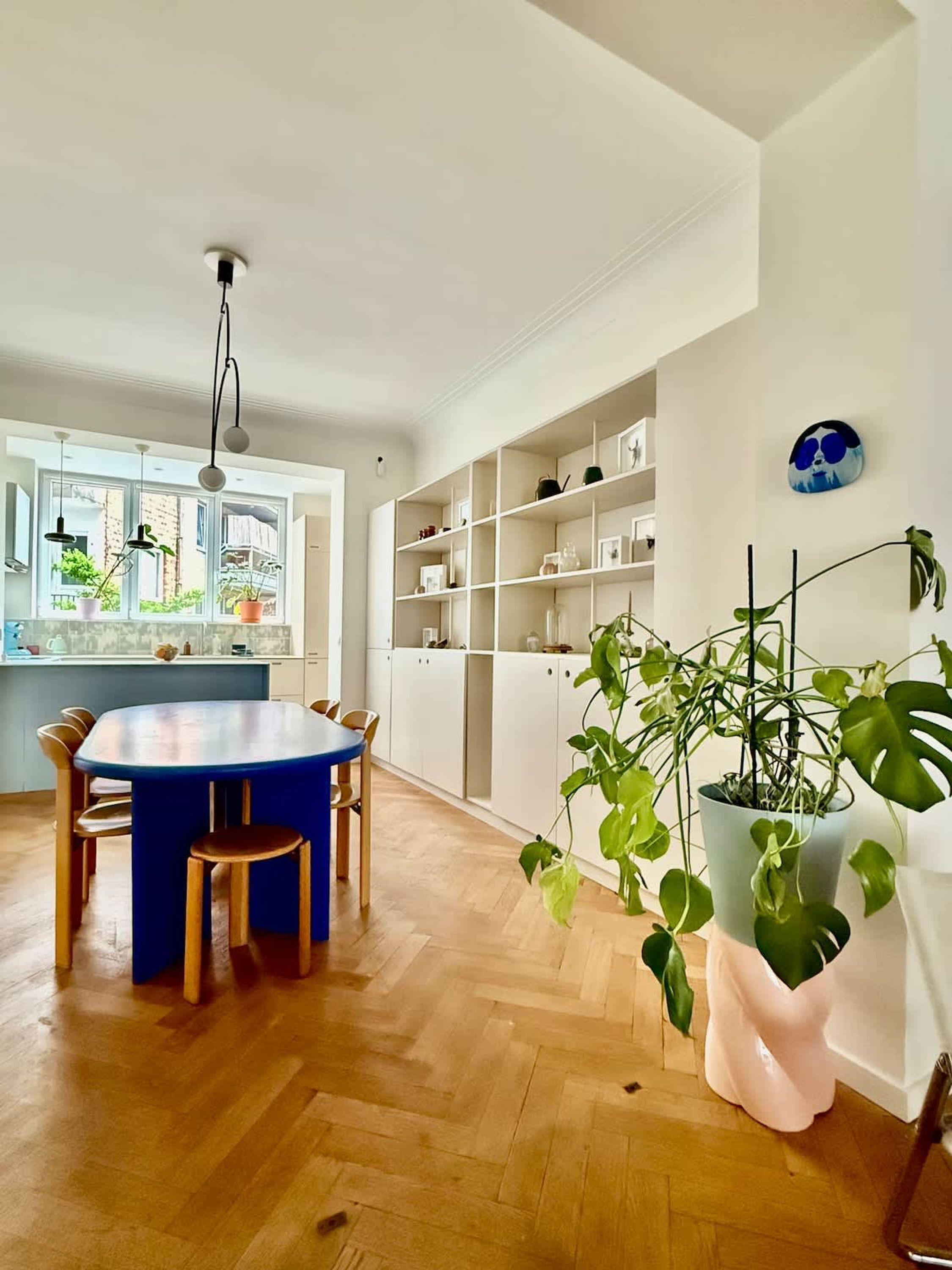 Een moderne keuken met een ronde blauwe tafel, witte kastjes en een groot raam.