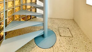 Un escalier en colimaçon avec une structure métallique bleue, un mur de verre à motifs géométriques et un sol à motifs pointillés.