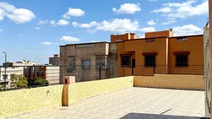A rooftop terrace with a tiled floor, a yellow wall, and a building with a brown facade. - Villa With Pool Rooftop Near Amelkis and Al Maaden Golf Courses Route de Ouarzazate Area (Marrakech)