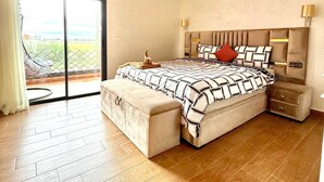 A bedroom with a large bed, a bench, a nightstand, a wall-mounted lamp, and a sliding glass door leading to a balcony. - Villa With Pool Rooftop Near Amelkis and Al Maaden Golf Courses Route de Ouarzazate Area (Marrakech)
