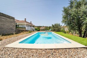 A rectangular swimming pool with a pebble border, surrounded by a grassy area and a tree.