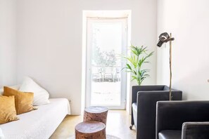 A bedroom with a bed, two wooden stools, a black chair, a floor lamp, and a potted plant.