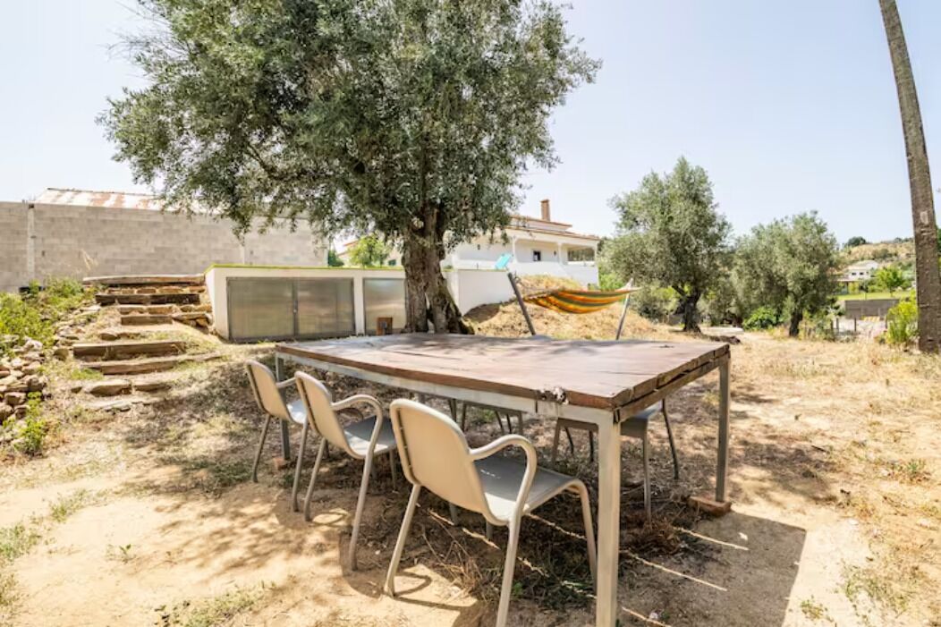 An outdoor dining area with a table and chairs, a hammock, and a tree.