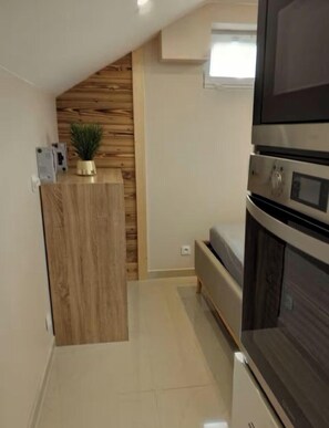 A compact kitchen with a wooden accent wall, a built-in oven, and a small seating area. - Cozy studio, ideal for a business trip or a weekend getaway” (Albertville)