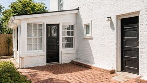 A white brick building with a black door, a small window, and a brick patio. - The Courtyard Cottage|2BD 1BH|Private Garden Suite (Columbus)