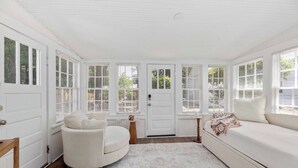 A room with a white door, a round white chair, a white sofa, and a small table with a candle. - The Courtyard Cottage|2BD 1BH|Private Garden Suite (Columbus)