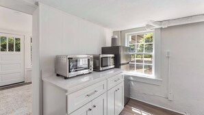 A kitchen with white cabinetry, a built-in oven, a microwave, and a window providing natural light. - The Courtyard Cottage|2BD 1BH|Private Garden Suite (Columbus)