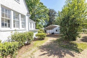 A white building with a covered porch and a dirt path leading to a garage.