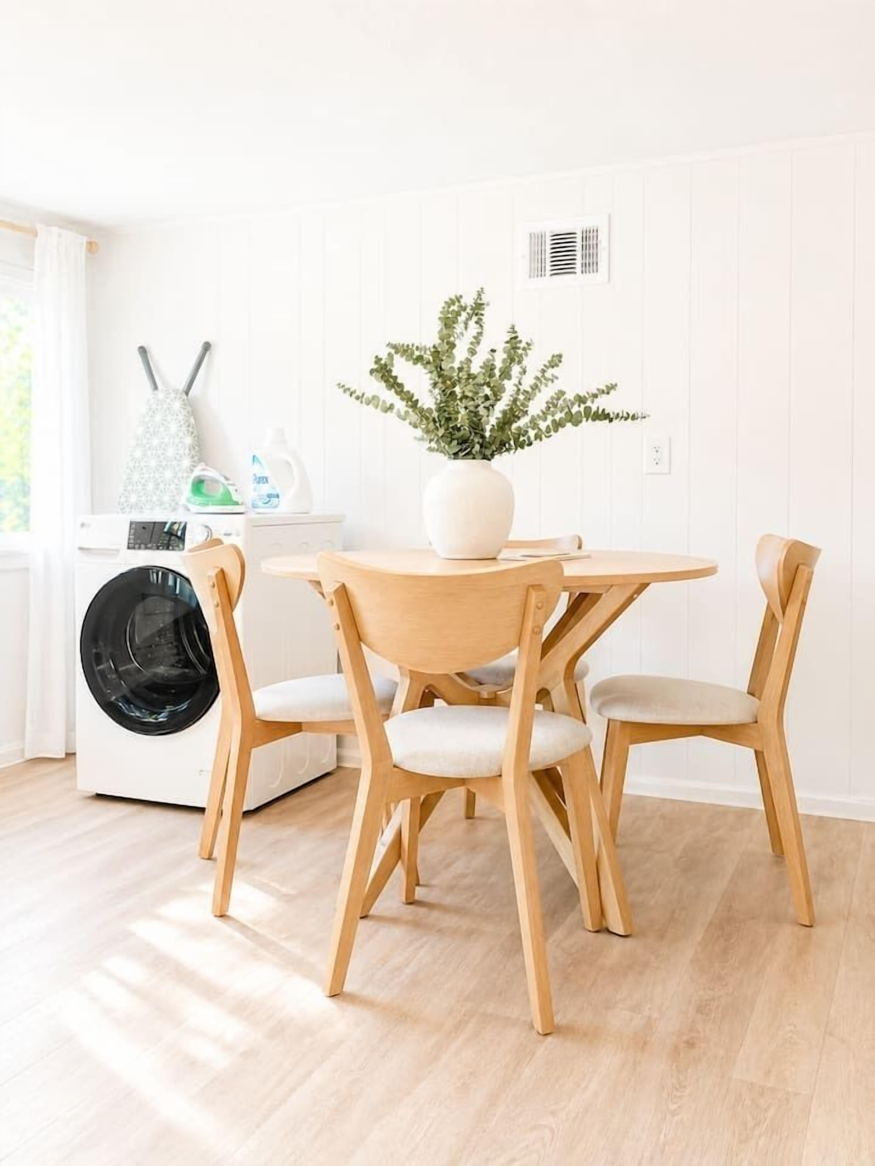 Une cuisine propre et moderne, avec une table ronde en bois, deux chaises, un lave-linge et une plante en pot.