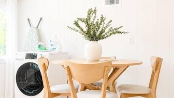 Une cuisine propre et moderne, avec une table ronde en bois, deux chaises, un lave-linge et une plante en pot.