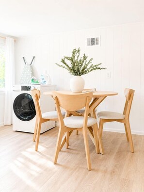 Una cocina moderna y limpia con una mesa redonda de madera, dos sillas, una lavadora y una planta en maceta.