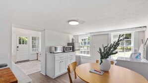 A modern kitchen with white cabinetry, a microwave, and a toaster. There is a dining table with chairs and a vase with a plant. - The Courtyard Cottage|2BD 1BH|Private Garden Suite (Columbus)