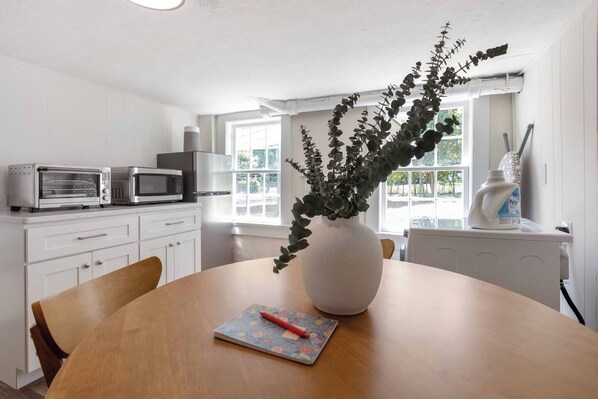 A modern kitchen with white cabinetry, a dining table with a vase of greenery, and a microwave oven.