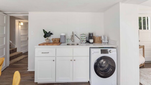 A compact kitchen with a built-in washing machine, a sink, and a countertop with various items. - The Courtyard Cottage|2BD 1BH|Private Garden Suite (Columbus)