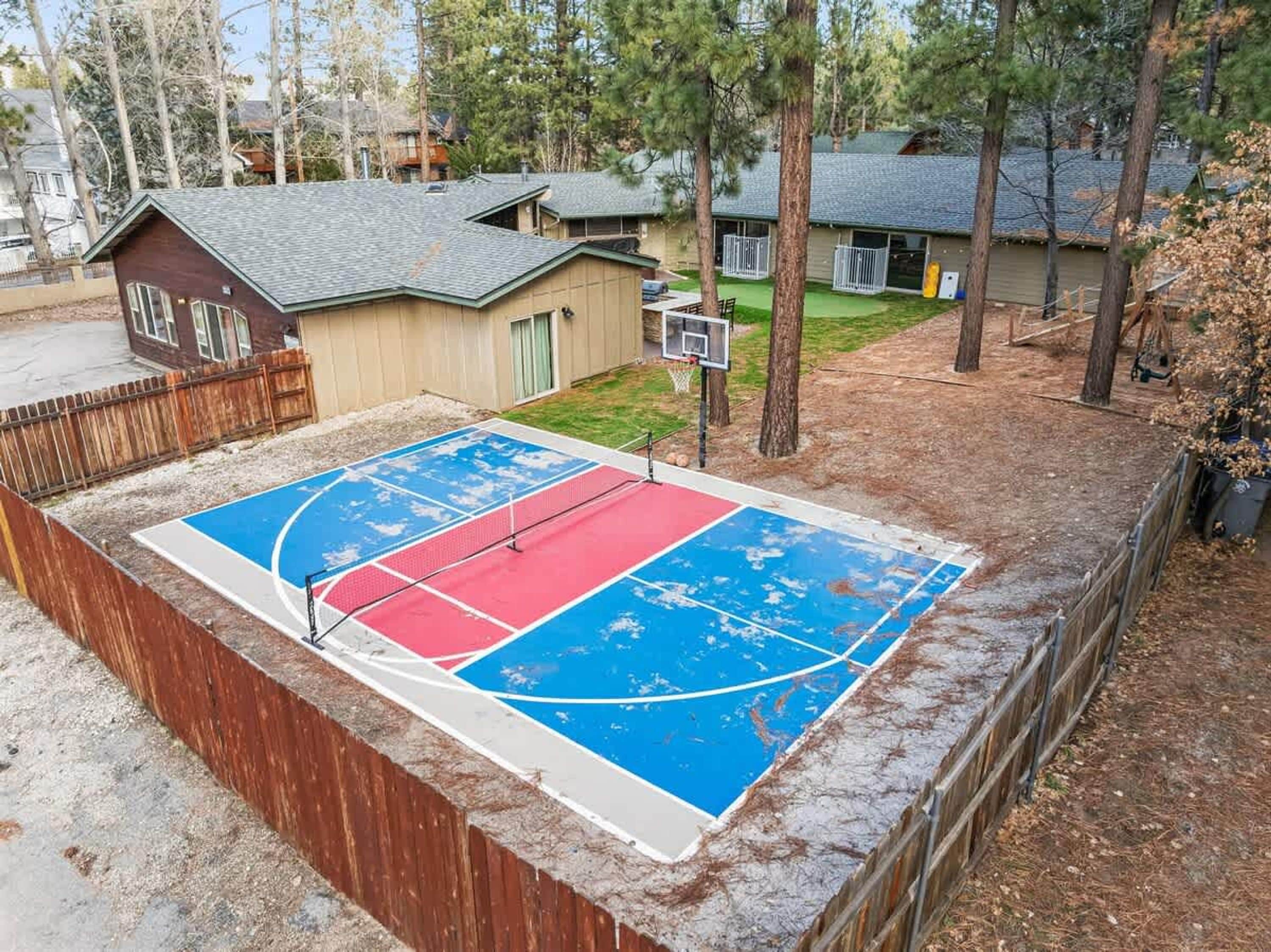 Un terrain de basket-ball entouré d’une clôture en bois, avec un petit abri et des arbres en arrière-plan.