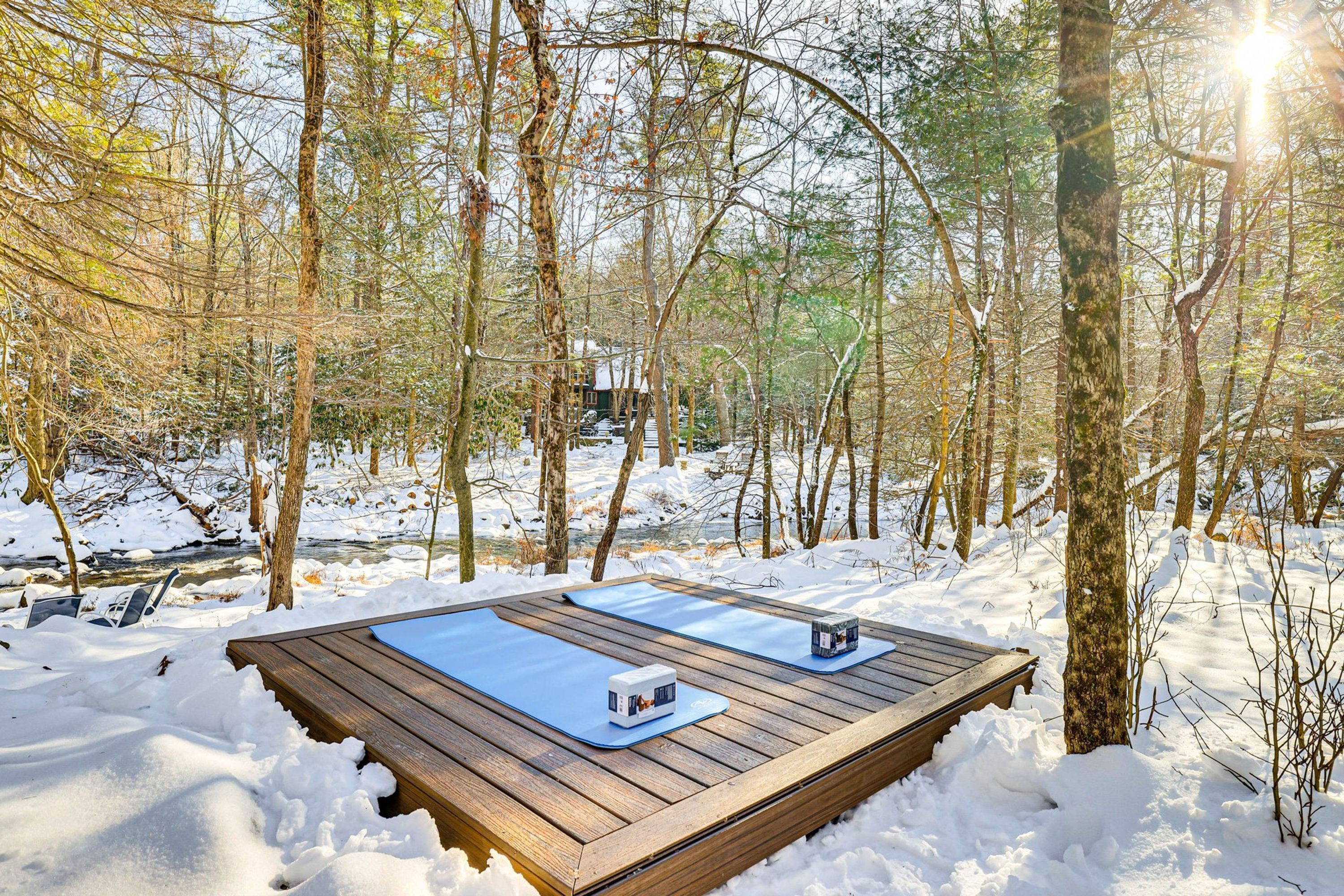 Un ponte di legno con due tappetini blu e due scatole bianche, circondato da neve e alberi.
