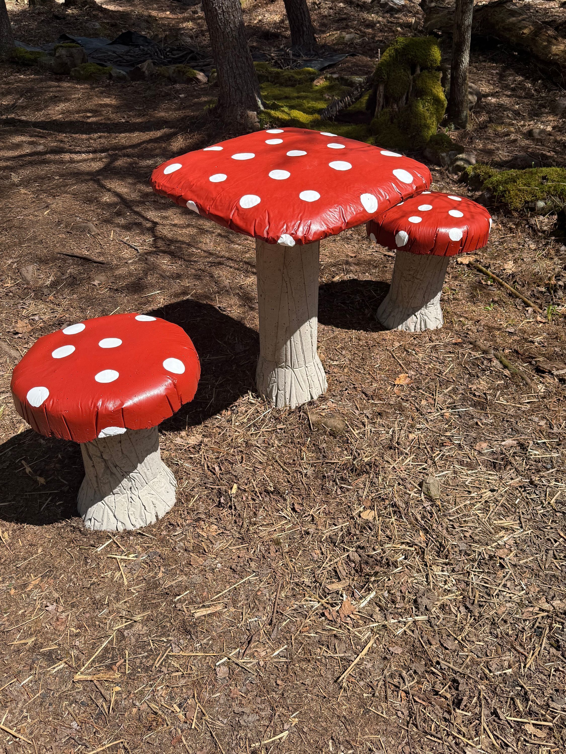 Ein pilzförmiger Tisch mit roter Kappe und weißen Punkten auf einem Waldboden.