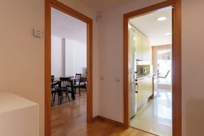 A hallway leading to a dining area with a wooden floor and a kitchen with light-colored cabinets and a refrigerator. - Garden & Pool apartment 8 persons (Tossa de Mar)