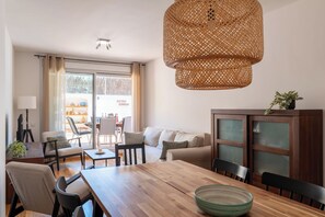 A modern living room with a wooden dining table, chairs, a sofa, and a large woven light fixture. - Garden & Pool apartment 8 persons (Tossa de Mar)