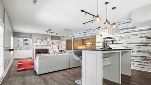 Una cucina moderna con mobili bianchi, un'isola centrale, illuminazione a sospensione e una parete in stile rustico.