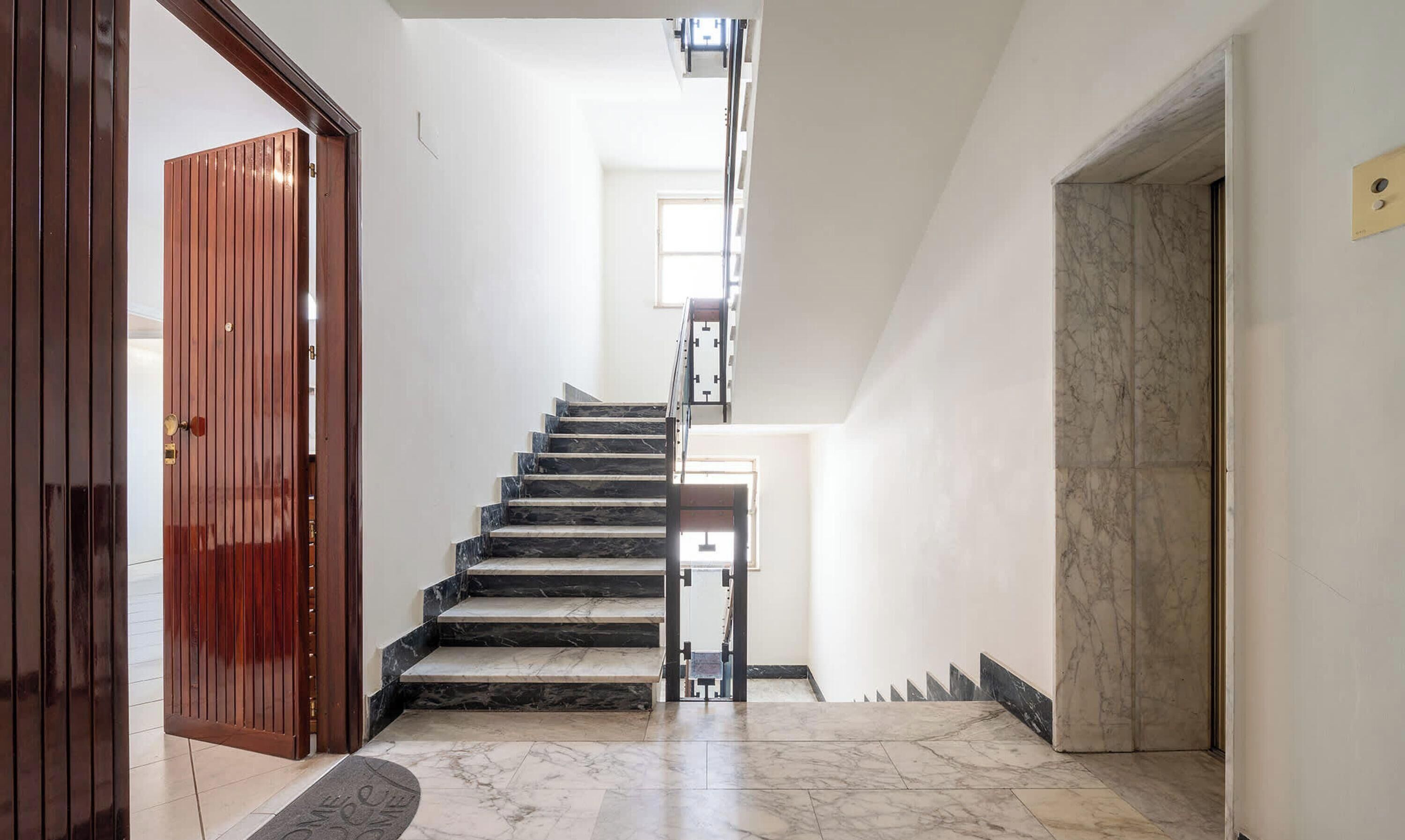 Eine Treppe mit Marmorstufen führt zu einer Zwischenebene, links eine Holztür und rechts eine Marmorwand.