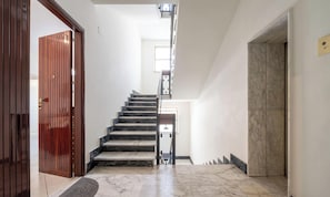 Una escala de marbre que condueix a una plataforma, una porta de fusta a l'esquerra i una paret de marbre a la dreta.