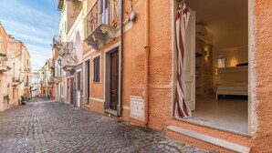 A cobblestone street leading to a building with a large window, a door, and a small balcony. - Ca Rouge - Modern Bright 3BR Boutique Retreat in the Heart of Carloforte (Carloforte)