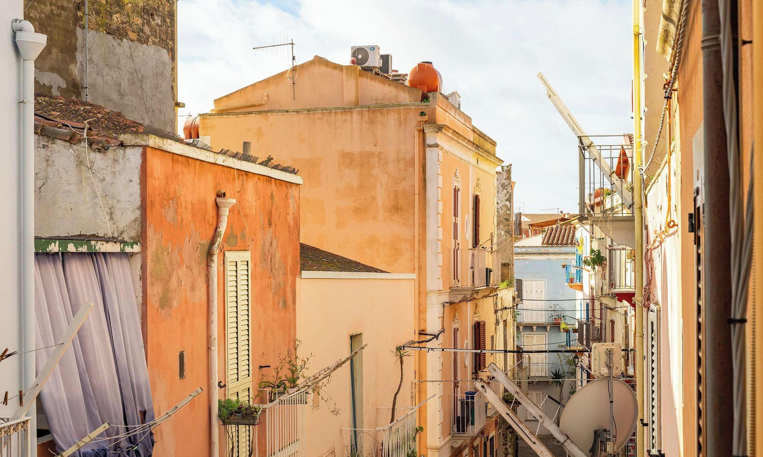 Une rue étroite bordée d’immeubles, dont certains présentent des balcons et des fenêtres apparents, ainsi que des échafaudages de construction.