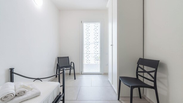 A hotel room with a bed, two chairs, a small table, and a door with a frosted glass panel. - Modern 2BR Retreat in Pula - Bright Quiet (Pula)