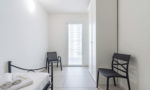 A hotel room with a bed, two chairs, a door with a frosted glass panel, and a tiled floor. - Modern 2BR Retreat in Pula - Bright Quiet (Pula)