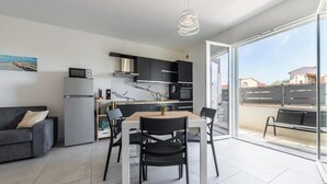 A modern kitchen with a dining area, a sofa, and a view through large glass doors. - Modern 2BR Retreat in Pula - Bright Quiet (Pula)
