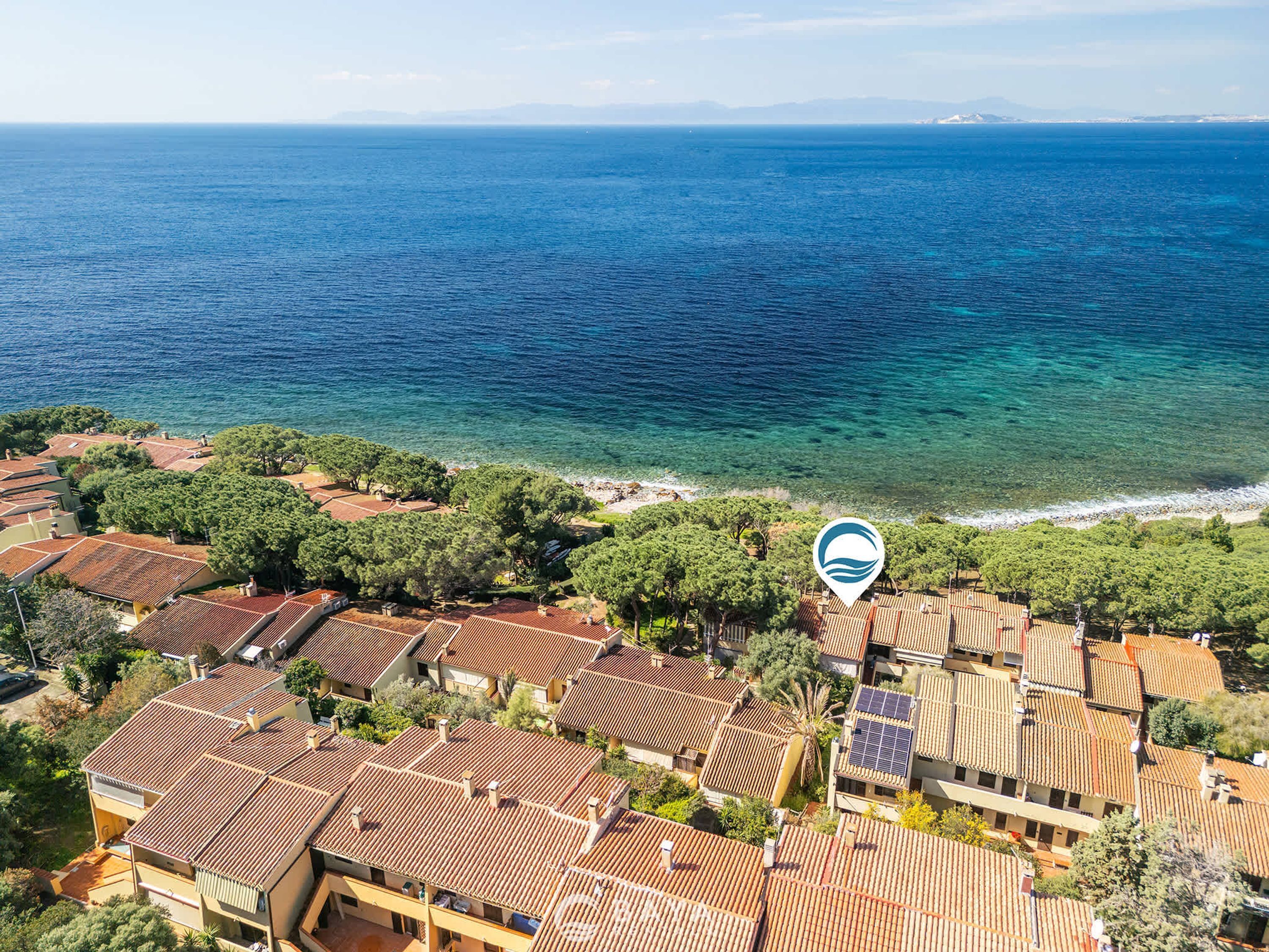 A coastal residential area with terracotta-roofed houses, a clear view of the sea, and a prominent location marker.