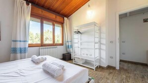 A bedroom with a bed, a radiator, a window with curtains, a white shelf unit, and a door. - Seaside Villa Apartment With Beach Access (Quartu Sant'Elena)